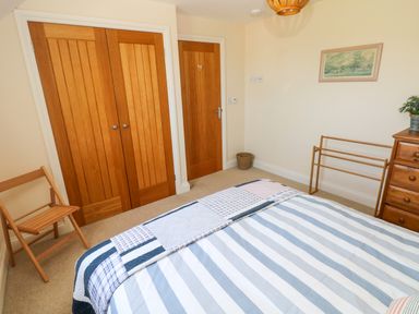 A bedroom with a striped bedspread wooden wardrobe doors a folding chair a chest of drawers and a towel rack at Llain Gwynfor in St Davids