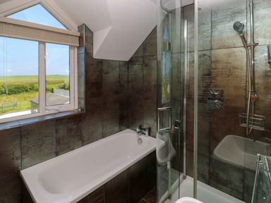 A bathroom with a bathtub and a glass-enclosed shower next to a window with a view of a garden at Llain Gwynfor in St Davids