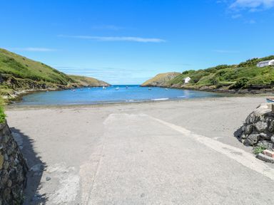 A sandy beach with boats in the water and hills on both sides at Llain Gwynfor in St Davids