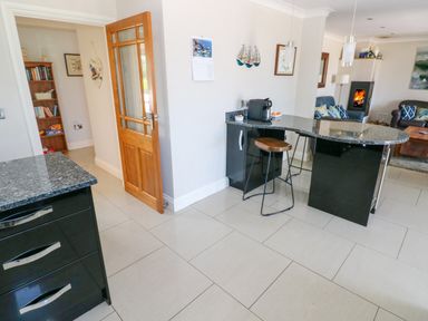 A kitchen with a granite countertop island and a stool and a living room with chairs and a fireplace at Llain Gwynfor in St Davids