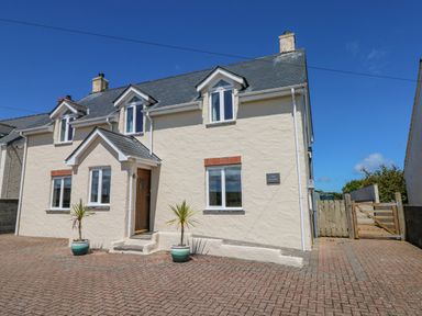 Exterior view of a two story cream house with a wooden front door and two potted plants on a brick driveway at Llain Gwynfor in St Davids