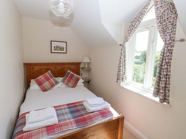 A bedroom with a double bed two plaid pillows folded towels on the bed and a window with patterned curtains at Llain Gwynfor in St Davids
