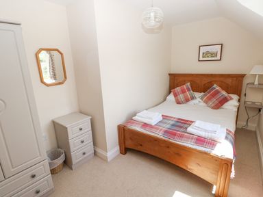 A bedroom with a wooden bed with plaid pillows and blanket two bedside tables a wall mirror and a wardrobe at Llain Gwynfor in St Davids