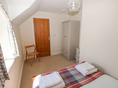 A bedroom with a bed with folded white towels a wooden chair a wardrobe and a wooden door at Llain Gwynfor in St Davids