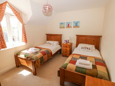 A bedroom with two single beds bedside table and window with orange curtains at Llain Gwynfor in St Davids
