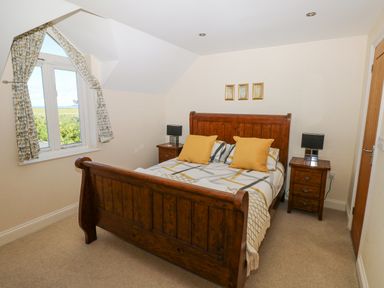A bedroom with a wooden bed frame yellow pillows bedside tables with lamps and a window with patterned curtains at Llain Gwynfor in St Davids
