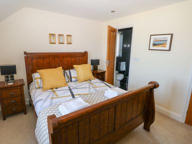 A bedroom with a wooden bed frame yellow pillows bedside tables with lamps and an open door to a bathroom at Llain Gwynfor in St Davids