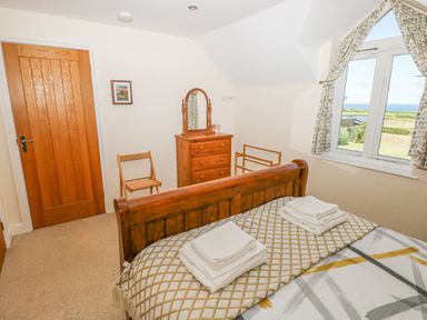 A bedroom with a wooden bed and dresser next to a window with curtains at Llain Gwynfor in St Davids