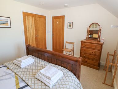 A bedroom with a wooden bed frame folded towels on the bed wooden doors a wooden chair a wooden dresser with a mirror and a wooden clothes rack at Llain Gwynfor in St Davids