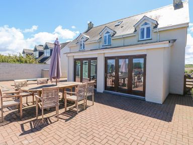 An outdoor patio area with a wooden dining table and chairs and a closed umbrella at Llain Gwynfor in St Davids
