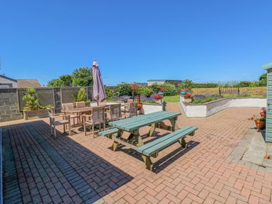 An outdoor patio with wooden dining table and chairs a green picnic table and an umbrella at Llain Gwynfor in St Davids