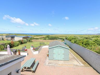 An outdoor area with a large garden shed a picnic table and views of fields and the sea at Llain Gwynfor in St Davids