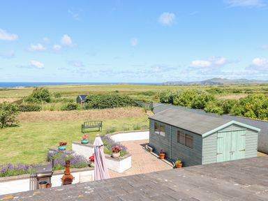 A garden with a green shed a bench flowers and a barbecue with an ocean view at Llain Gwynfor in St Davids