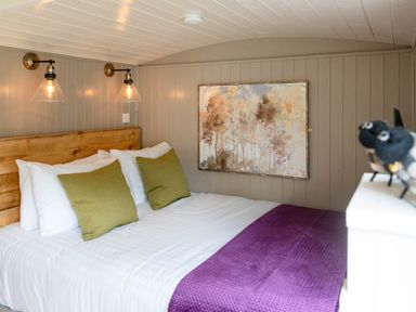 A bedroom with a bed with green pillows and a purple blanket wood paneled walls and a painting at Collen in Aberaeron