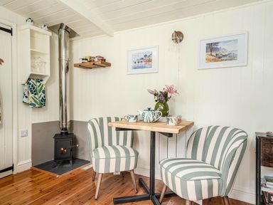 A small dining area with a wooden table and two striped chairs next to a wood stove with a metal chimney at Collen in Aberaeron