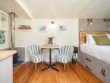 A small dining area with two striped chairs and a wooden table beside a bed at Collen in Aberaeron