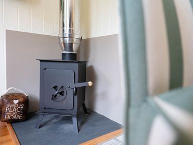 A black wood stove with a metal chimney pipe next to a doorstop with the text there's no place like home at Collen in Aberaeron