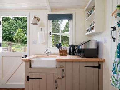 A kitchen with a sink stove kettle and air fryer next to a window and a door open to a garden at Collen in Aberaeron