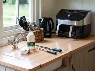 A kitchen countertop with a basket of utensils a kettle an air fryer a bottle of milk and a block of butter at Collen in Aberaeron