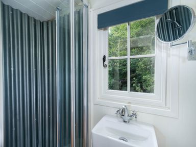 A bathroom with a white sink and a window with a blue blind next to a shower with corrugated metal walls at Collen in Aberaeron