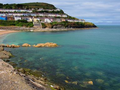 A coastal bay with clear turquoise water rocks and houses on a hillside at Collen Aberaeron