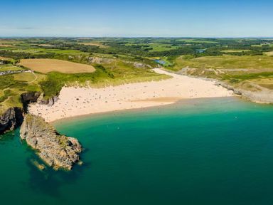 A sandy beach with people near a rocky coastline and green fields in the background at Collen in Aberaeron