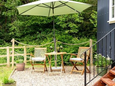 An outdoor seating area with two wooden chairs with cushions a small round table under a large umbrella and potted plants near a building at Bedwen in Aberaeron