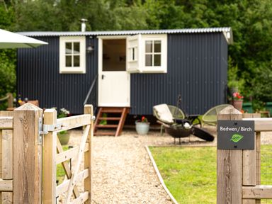 A small black cabin with white windows and door behind a wooden gate at Bedwen in Aberaeron