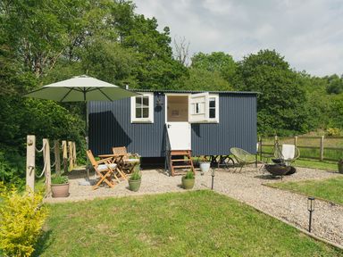 A small black shepherd hut with white windows and a door surrounded by gravel and outdoor furniture at Bedwen in Aberaeron