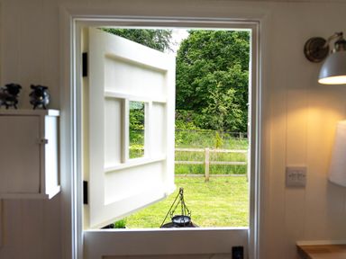 A half open white door looking out to a garden with grass and a wooden fence at Bedwen in Aberaeron