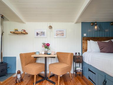 A small dining area with two orange chairs and a wooden table next to a bed with white bedding and wooden floors at Bedwen in Aberaeron