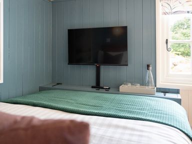 A bedroom with a wall mounted television a bed with a blue cover and a window at Bedwen in Aberaeron