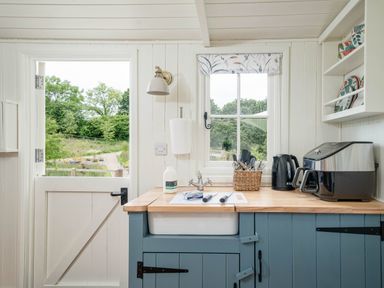 A kitchen with a half door open to a garden a sink with utensils a kettle an air fryer and shelves with plates at Bedwen in Aberaeron