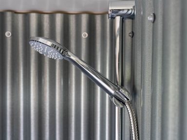 A metal shower head attached to a hose against a corrugated metal wall at Bedwen in Aberaeron