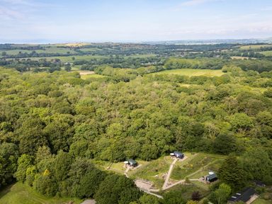 A wooded area with three small cabins and pathways surrounded by fields at Bedwen in Aberaeron