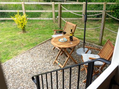 A small outdoor seating area with two wooden chairs and a round wooden table on gravel by a grassy fenced yard at Bedwen in Aberaeron