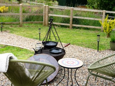 An outdoor seating area with two green chairs a small round table a fire pit with pans and a kettle on a gravel surface at Bedwen in Aberaeron
