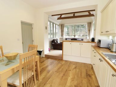 A kitchen with wooden floor and dining table next to a sitting area with sofas and large windows at The Folly in Belford