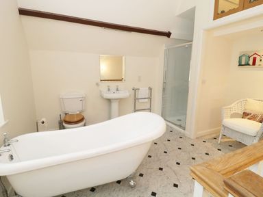 A bathroom with a freestanding bathtub toilet pedestal sink shower and a wicker chair at The Folly in Belford