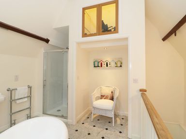 A bathroom with a shower, a white wicker chair with a cushion, and a bathtub at The Folly in Belford