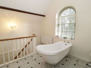 A bathroom with a white freestanding bathtub near a window and a staircase with wooden railing at The Folly in Belford