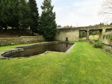 A stone pond surrounded by grass and trees with a stone wall and gate in the background at The Folly in Belford