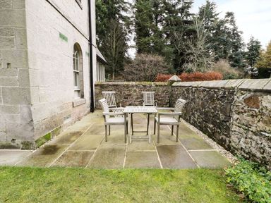 An outdoor patio with a table and four chairs surrounded by stone walls and trees at The Folly in Belford