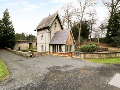 A small stone house with a slate roof and glass enclosed porch near a gravel driveway surrounded by trees and stone walls at The Folly in Belford