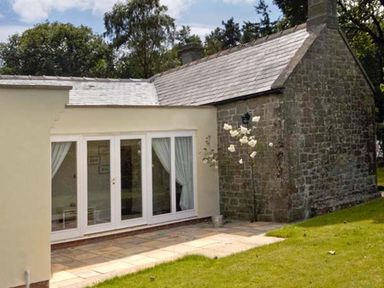 An exterior view of a house with a stone wall and glass doors opening to a patio with grass near Belford