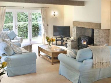 A living room with blue sofas a coffee table with flowers a fireplace and a television at The Lake Cottage Near Belford