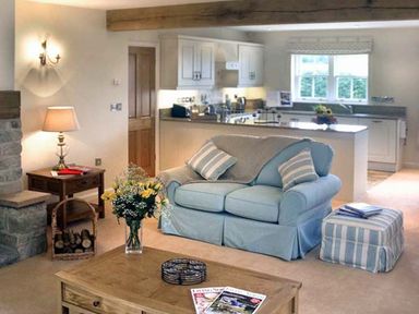 A living room with a blue sofa and striped ottoman next to a kitchen at The Lake Cottage Near Belford