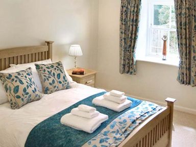 A bedroom with a wooden bed with blue patterned pillows and bed runner next to a window with matching curtains at The Lake Cottage Near Belford