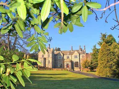A large stone house with a driveway and lawn surrounded by trees and greenery at The Hall in Belford
