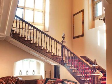 A wooden staircase with red carpet and a seating area with leather sofas and pillows under a window at The Hall in Belford